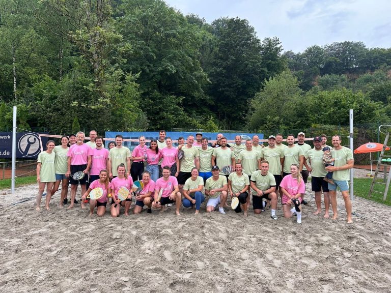 Gruppenfoto von Volleyballspielern in bunten Shirts auf Sandplatz.